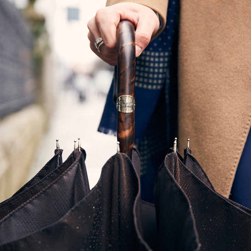 Hand holding the furled umbrella by its hickory handle with Pasotti plaque