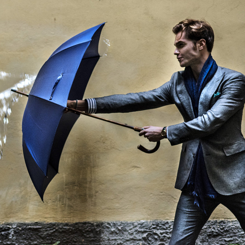 Man in a grey suit holding the open blue umbrella against the wind
