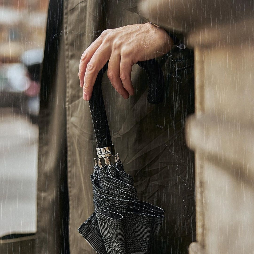 A man leans on a luxurious gray checkered Pasotti umbrella-cane with a leather braided handle