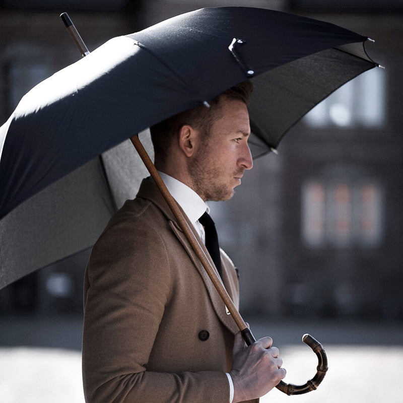 Man holding Pasotti black cane umbrella with bamboo handle in use