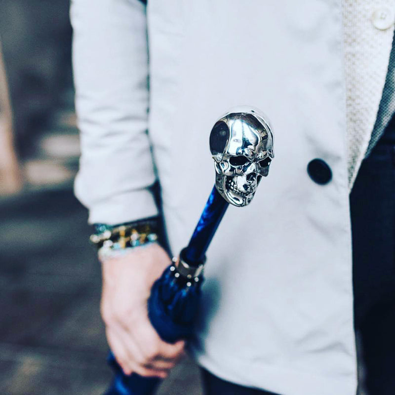 A blue umbrella with a skull in a man's hand