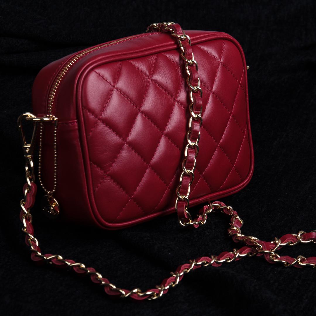 Tony Perotti Borsa CA006-01DR red quilted leather bag on black cloth with its strap — a gold chain woven through a strip of red leather