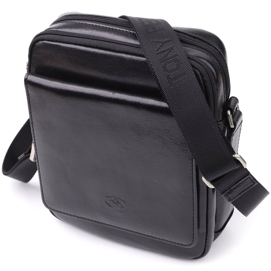 Three-quarter angled view of the closed Tony Perotti Italico 9148-17 black leather crossbody bag showing the front flap pocket, top zip compartments and black jacquard strap