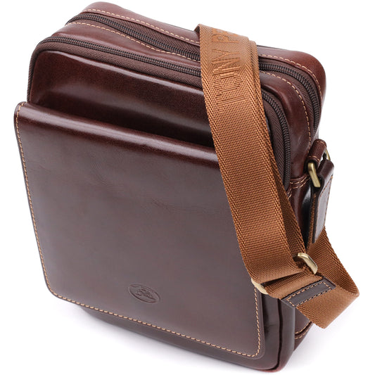 Three-quarter angled view of the closed Tony Perotti Italico 9148-17 dark brown leather crossbody bag showing the front flap pocket, top zip compartments and tan jacquard strap