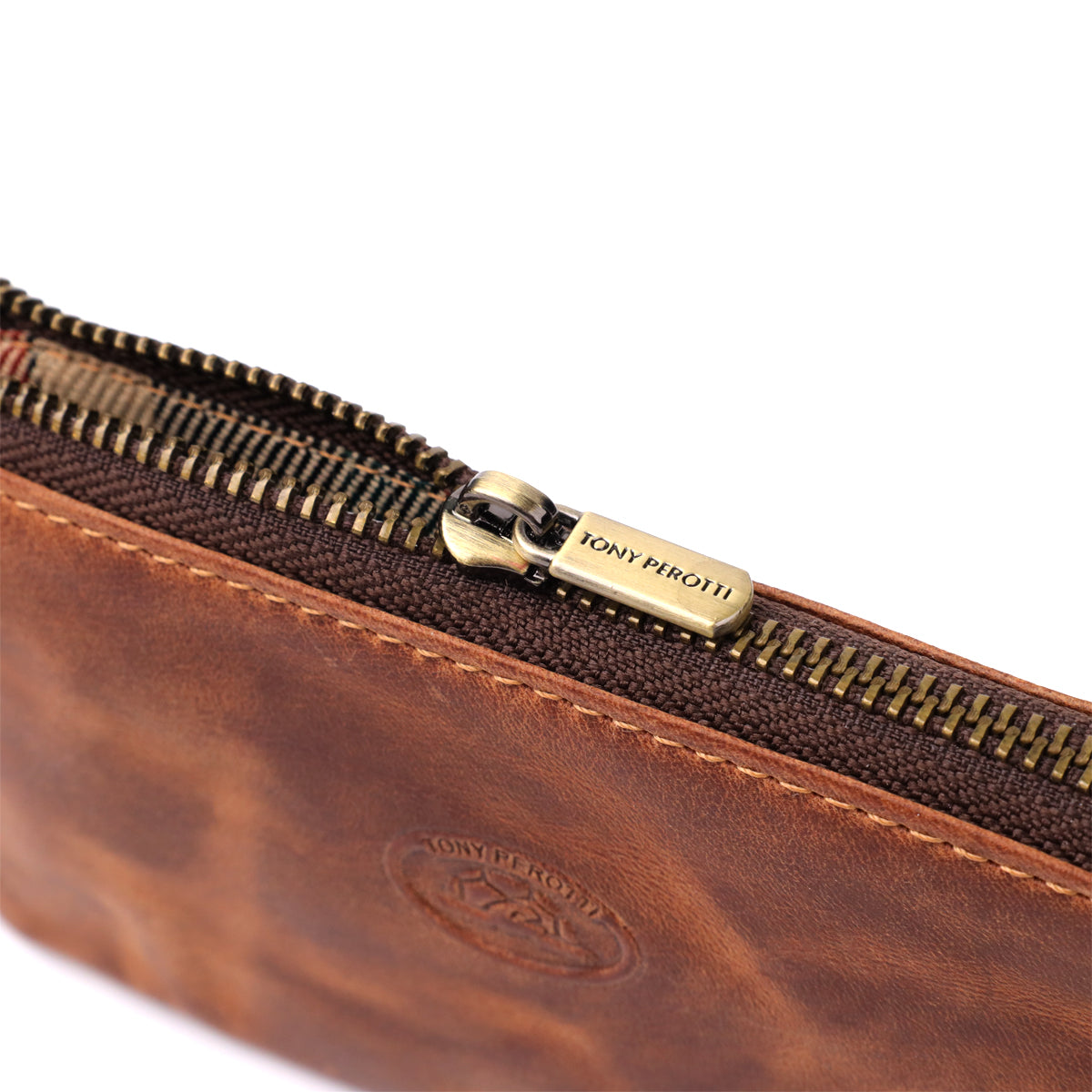 Macro close-up of the zip on the Tony Perotti Arno 3350 whisky key case — antique brass teeth and a pull tab stamped Tony Perotti