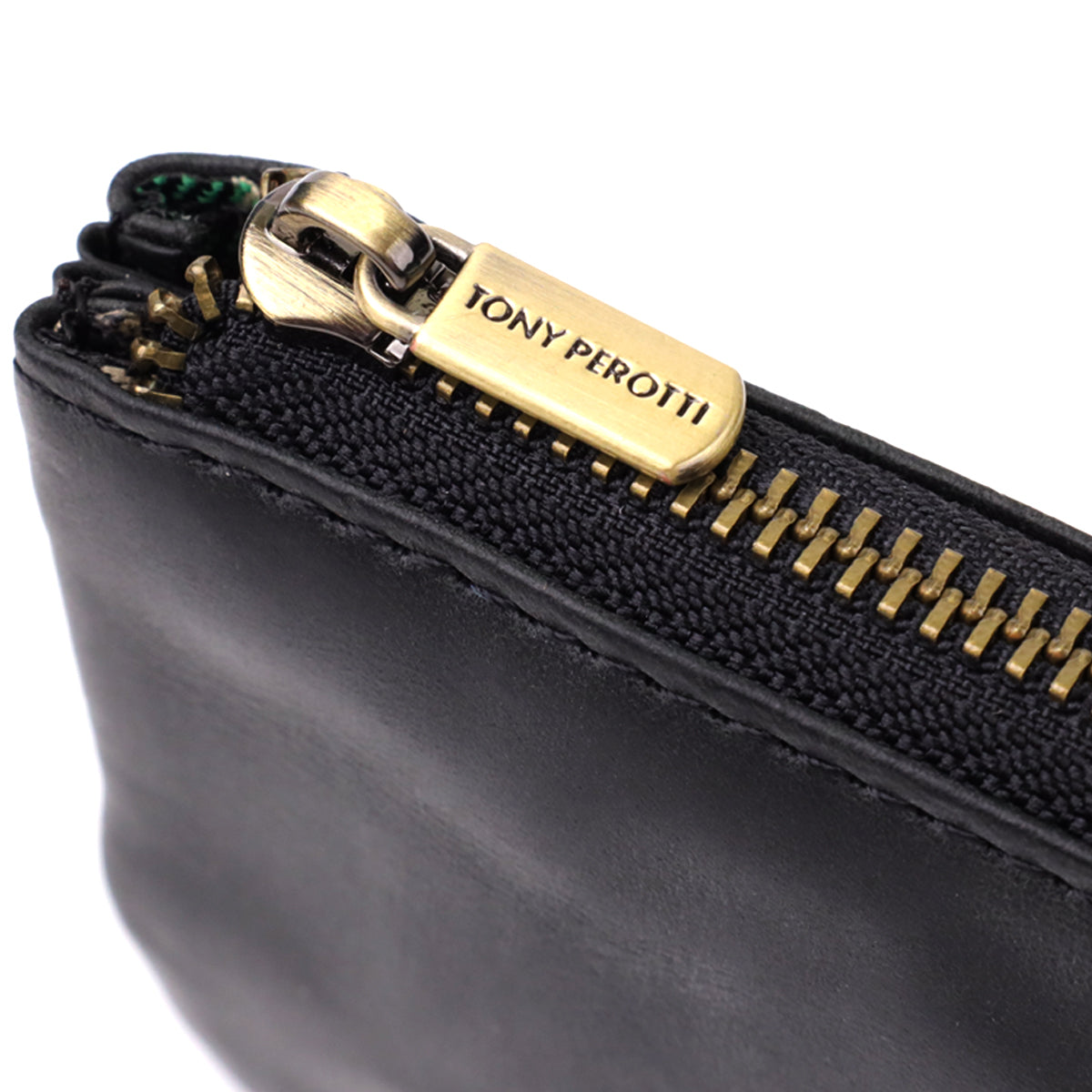 Macro close-up of the zip on the Tony Perotti Arno 3350 nero key case — antique brass teeth and a pull tab stamped Tony Perotti