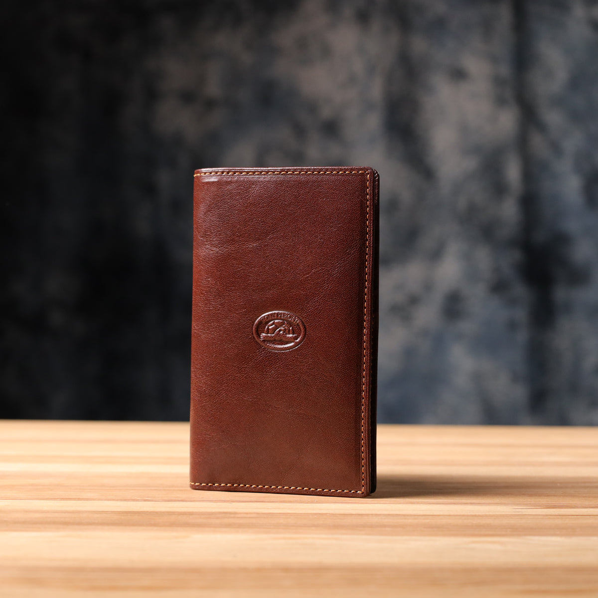 Tony Perotti Italico 1438 moro dark brown leather coat wallet standing on a wooden surface against a dark textured background