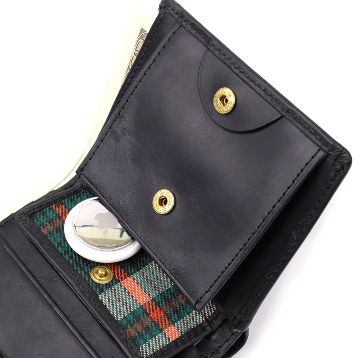 Macro close-up of the snap coin pocket on the Tony Perotti Arno 1165 nero wallet — tartan lining inside, shown holding an Apple AirTag