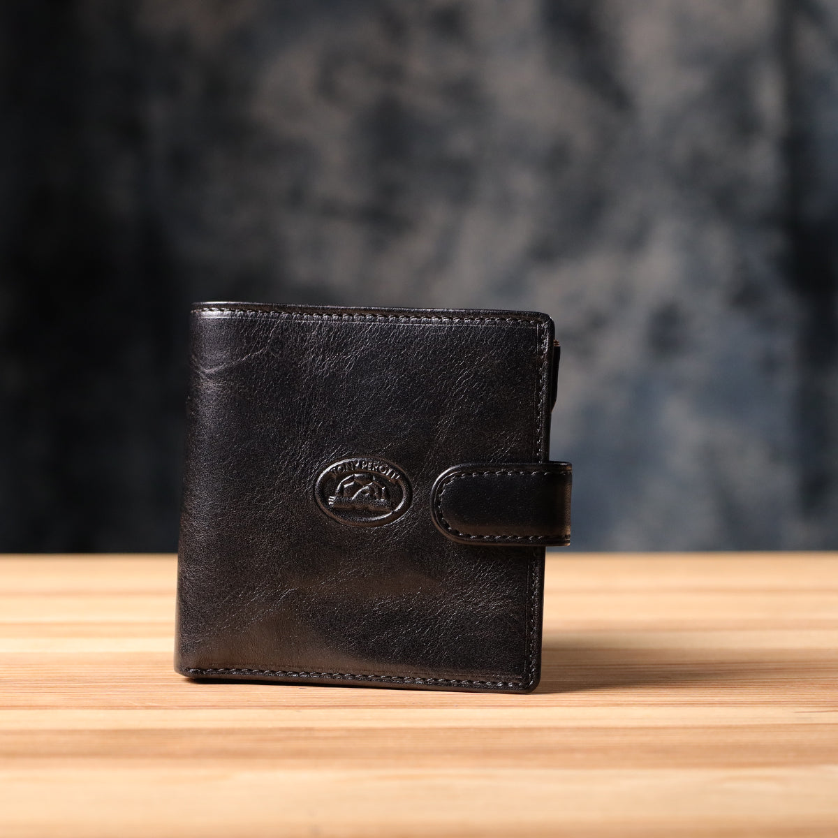 Tony Perotti Italico 1256 nero black leather compact wallet standing on a wooden surface against a dark textured background