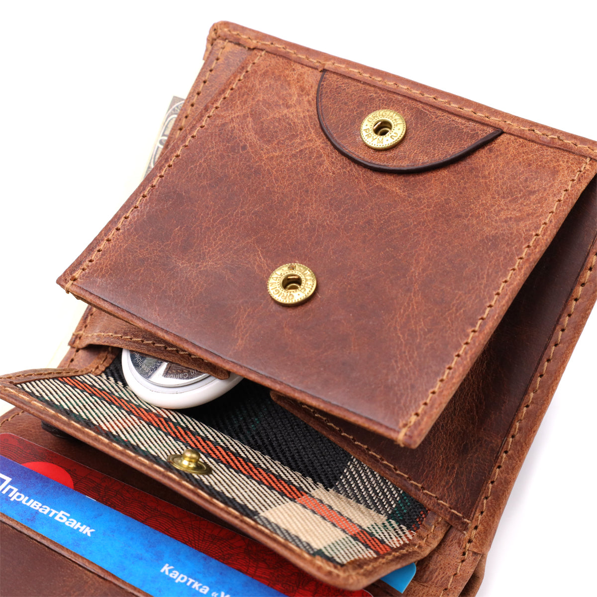 Macro close-up of the snap coin pocket on the Tony Perotti Arno 1165 whisky wallet — tartan lining inside, shown holding an Apple AirTag beside a bank card