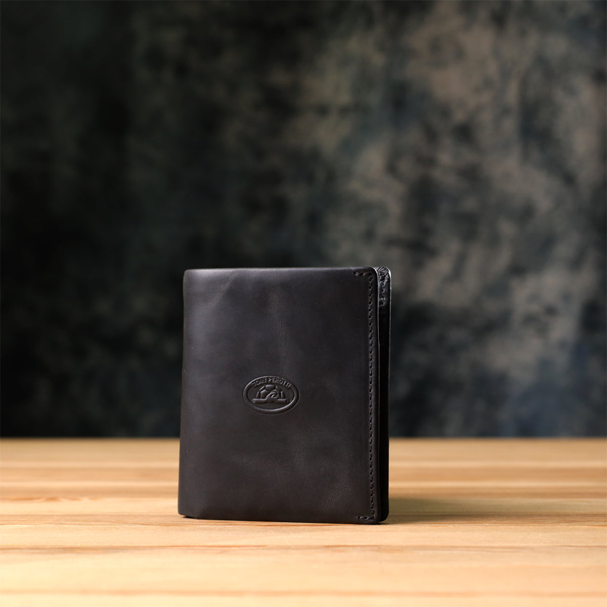 Tony Perotti Arno 1165 nero black leather bifold wallet standing on a wooden surface against a dark textured background