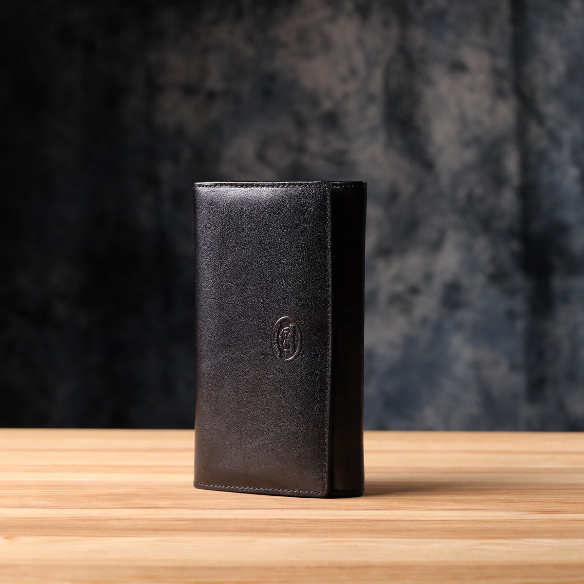 Tony Perotti Italico 1073 nero black leather flap wallet standing on a wooden surface against a dark textured background