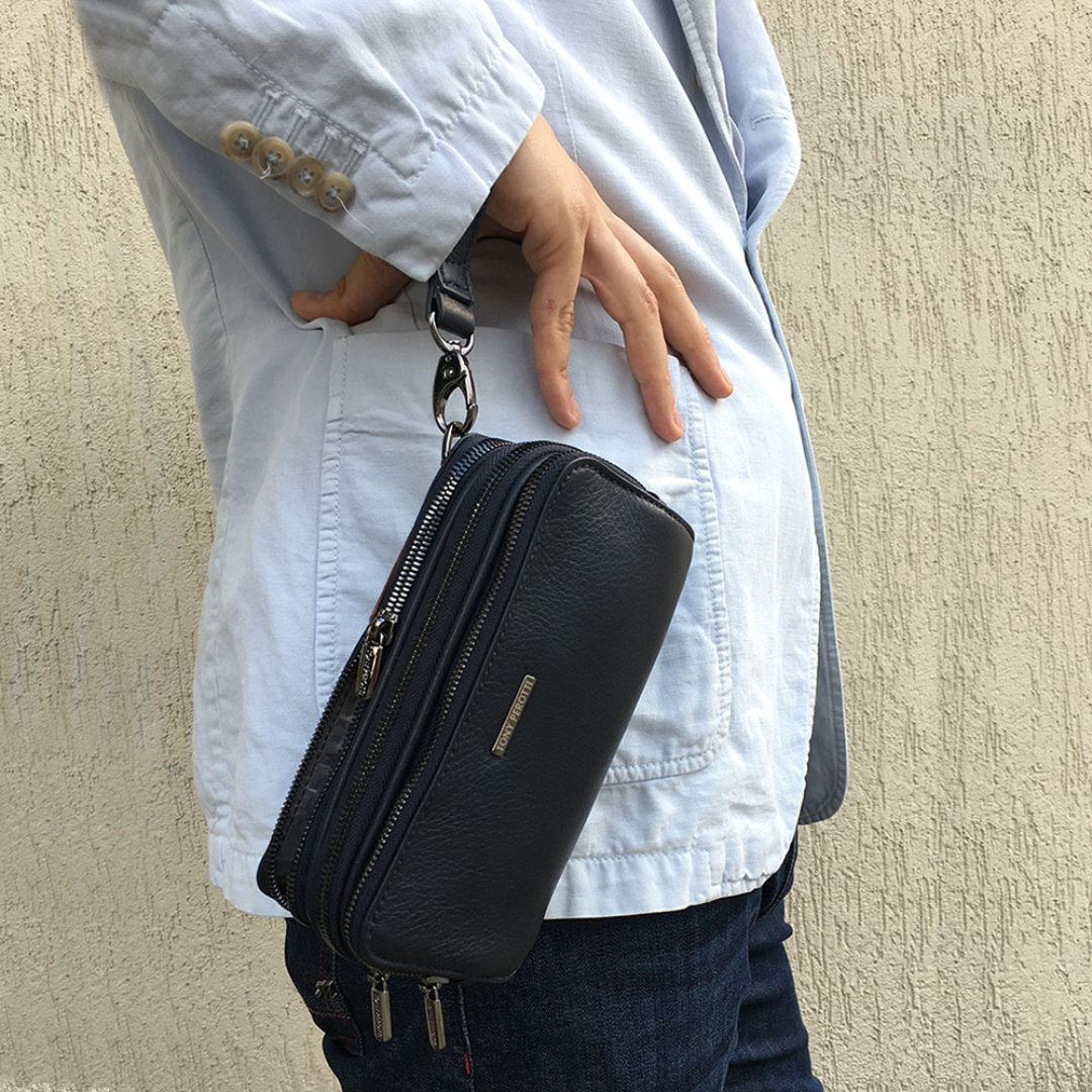 Black Tony Perotti clutch carried at the hip on its leather wrist strap