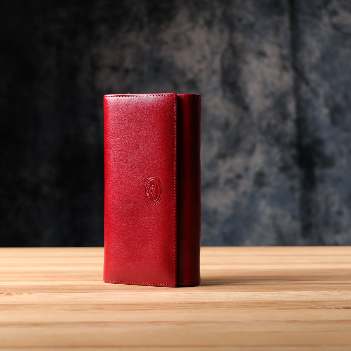 Tony Perotti Italico 1911 rosso red leather flap wallet standing on a wooden surface against a dark textured background