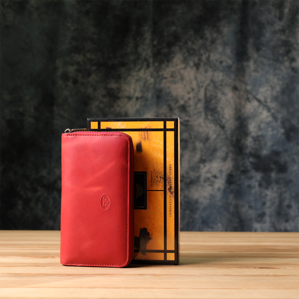 Tony Perotti Arno 2250 rosso red leather wallet standing next to its marbled orange and black printed gift box on a wooden surface