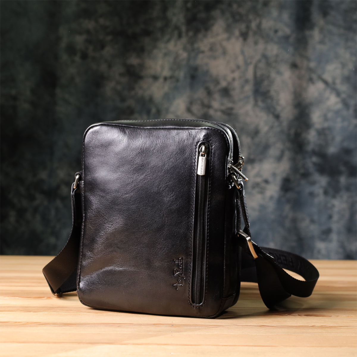 Side angled view of the Italico 9148-17 black bag on a wood surface, showing the front zip pocket and strap