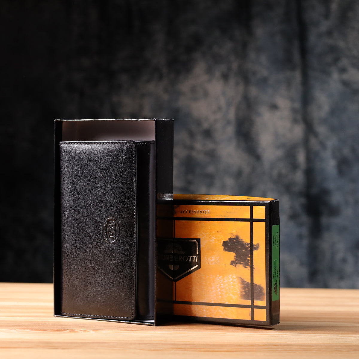Tony Perotti Italico 1073 nero black leather flap wallet standing next to its open marbled orange and black printed gift box on a wooden surface