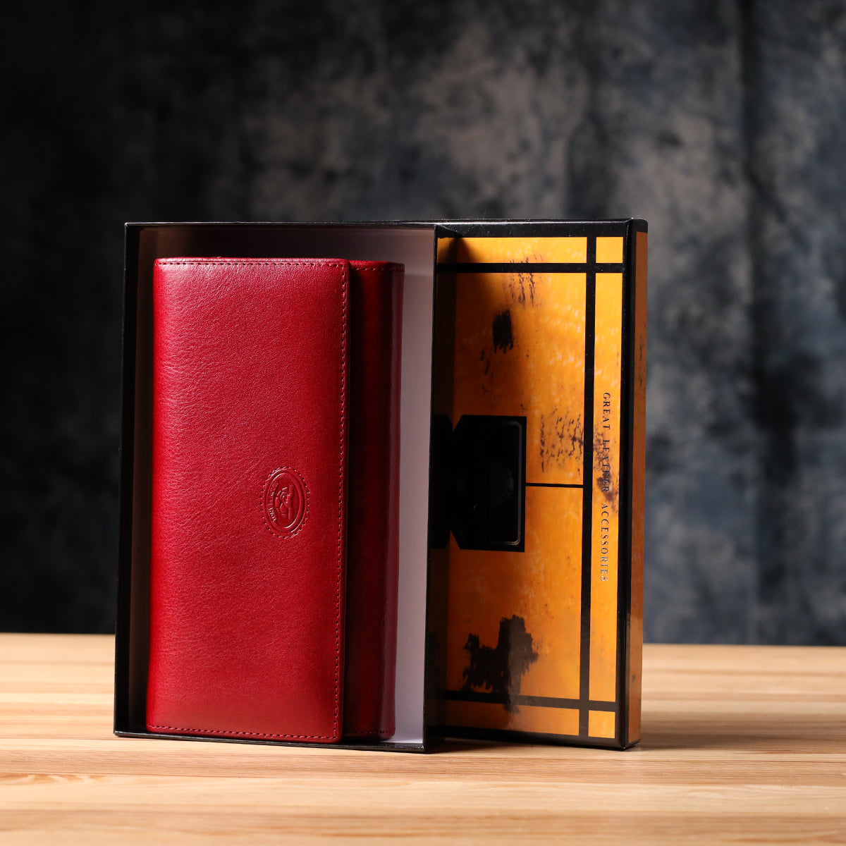 Tony Perotti Italico 1911 rosso red leather flap wallet standing in its open marbled orange and black printed gift box on a wooden surface
