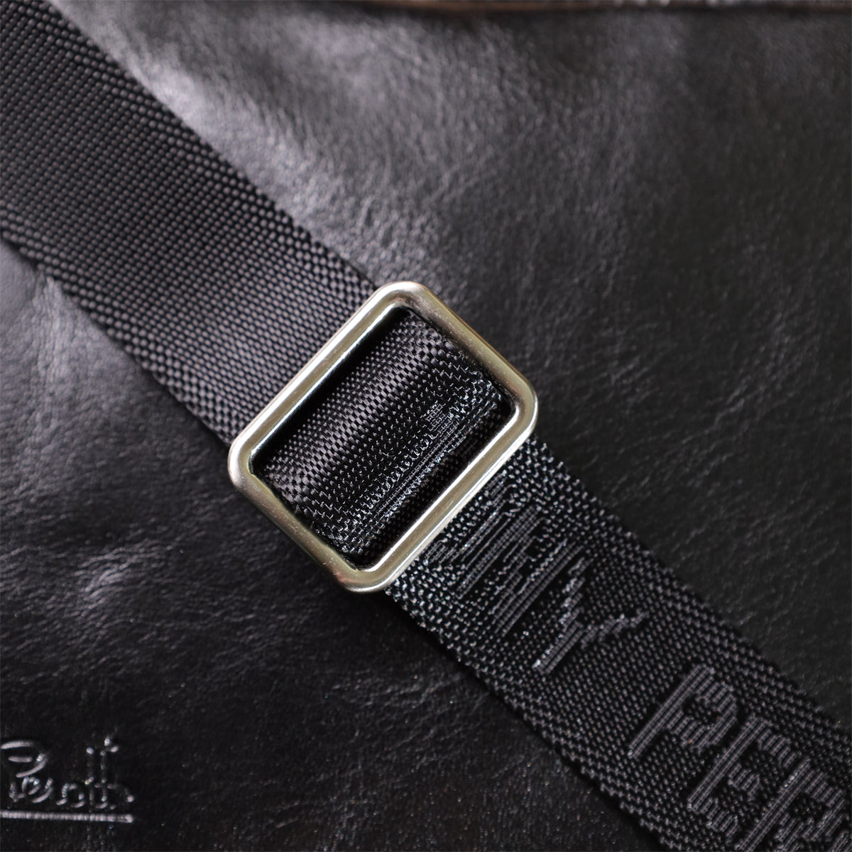 Macro shot of the strap's metal slide buckle on the Italico 9148-17 black bag with TONY PEROTTI woven into the webbing