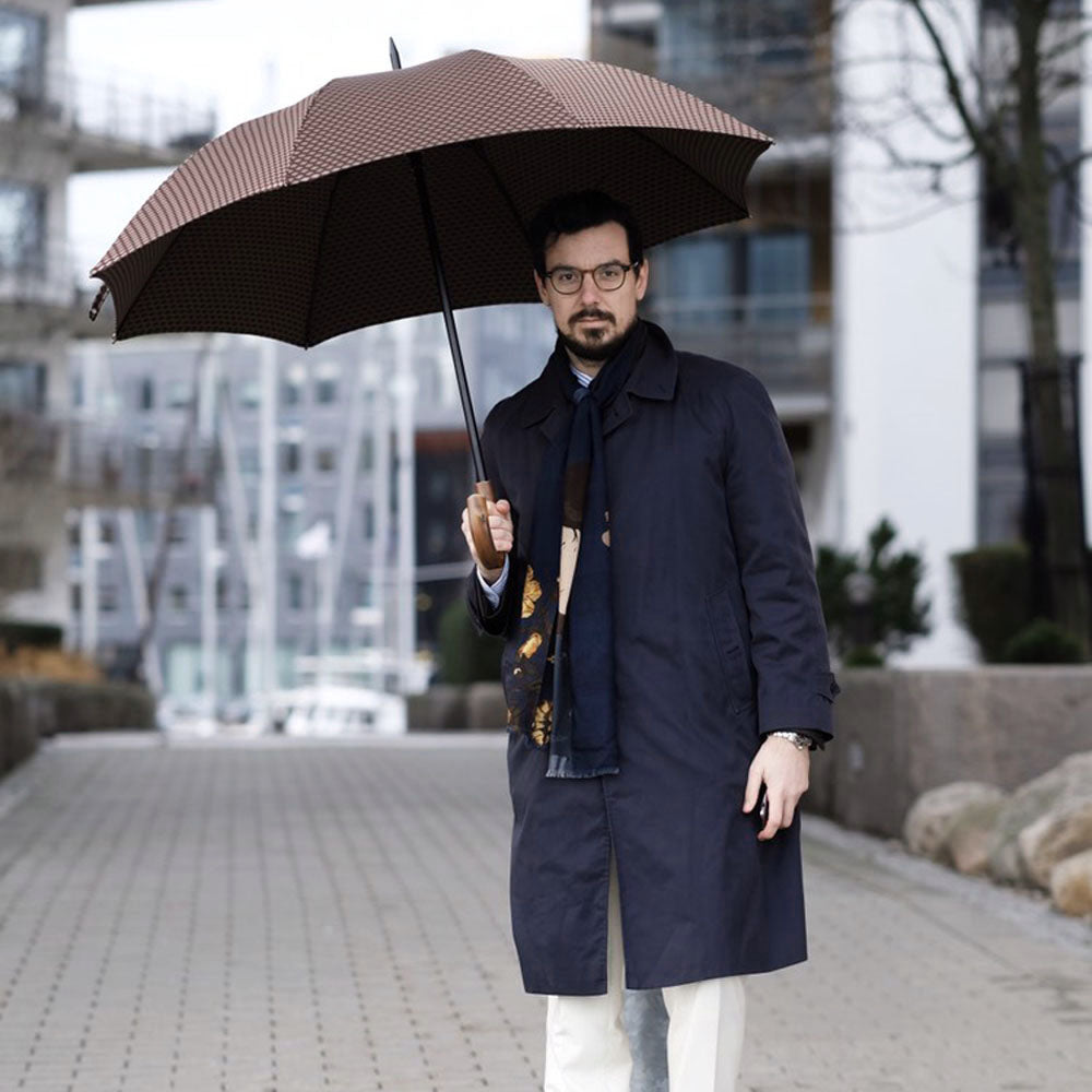 Man in a navy coat holding the open brown geometric umbrella on a city street
