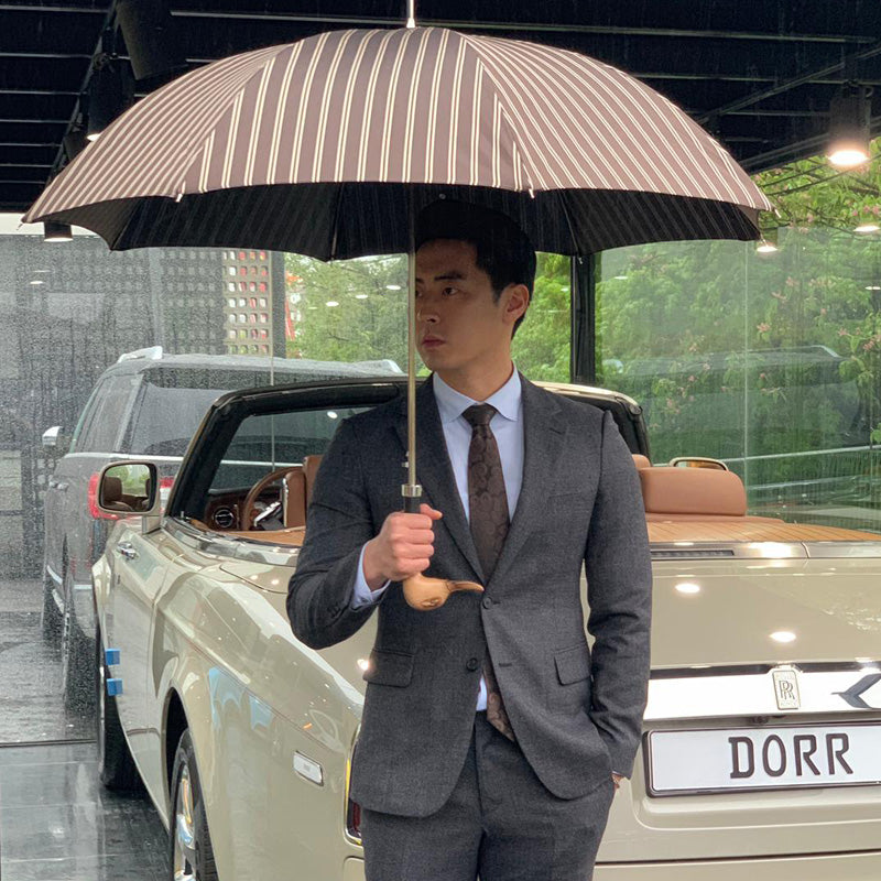 Man in a grey suit standing under the open brown striped umbrella, holding the duck handle
