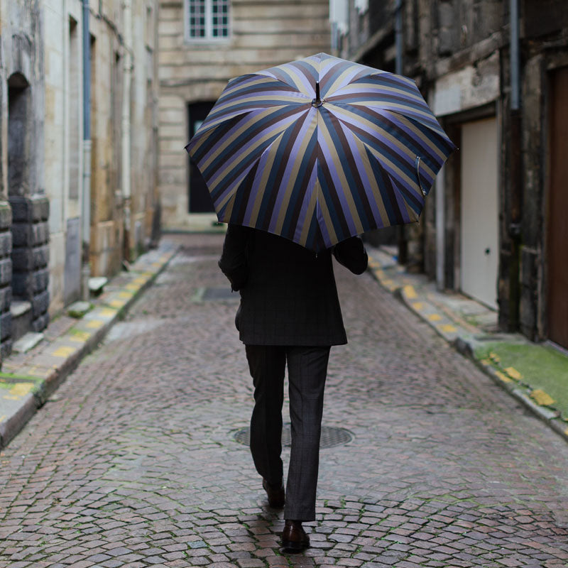 Man seen from behind under the open striped umbrella on a cobbled street