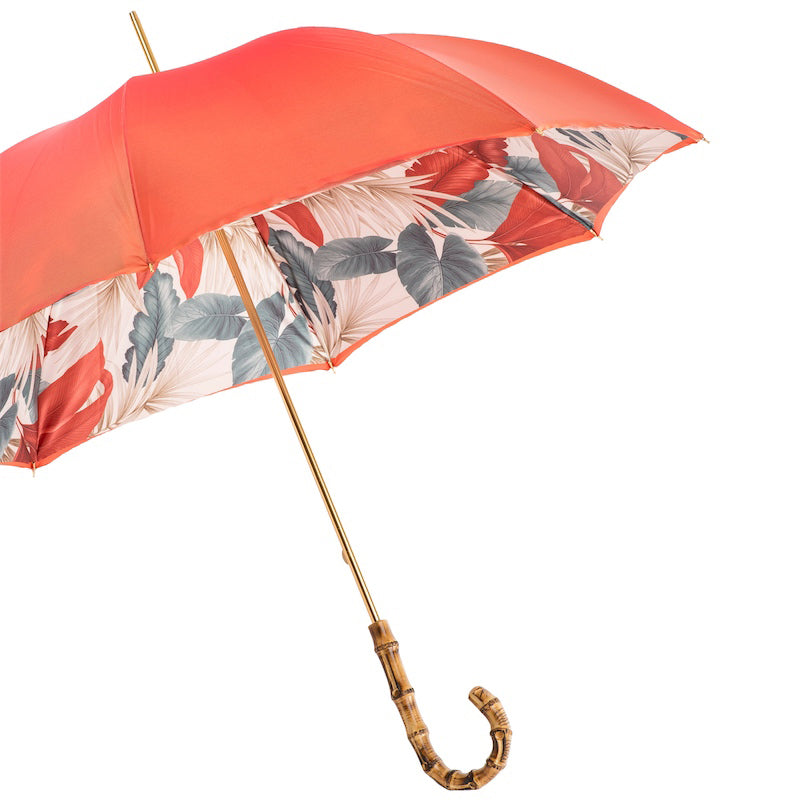 Open coral umbrella from the side showing the tropical leaf print inside the canopy and gold-tone shaft