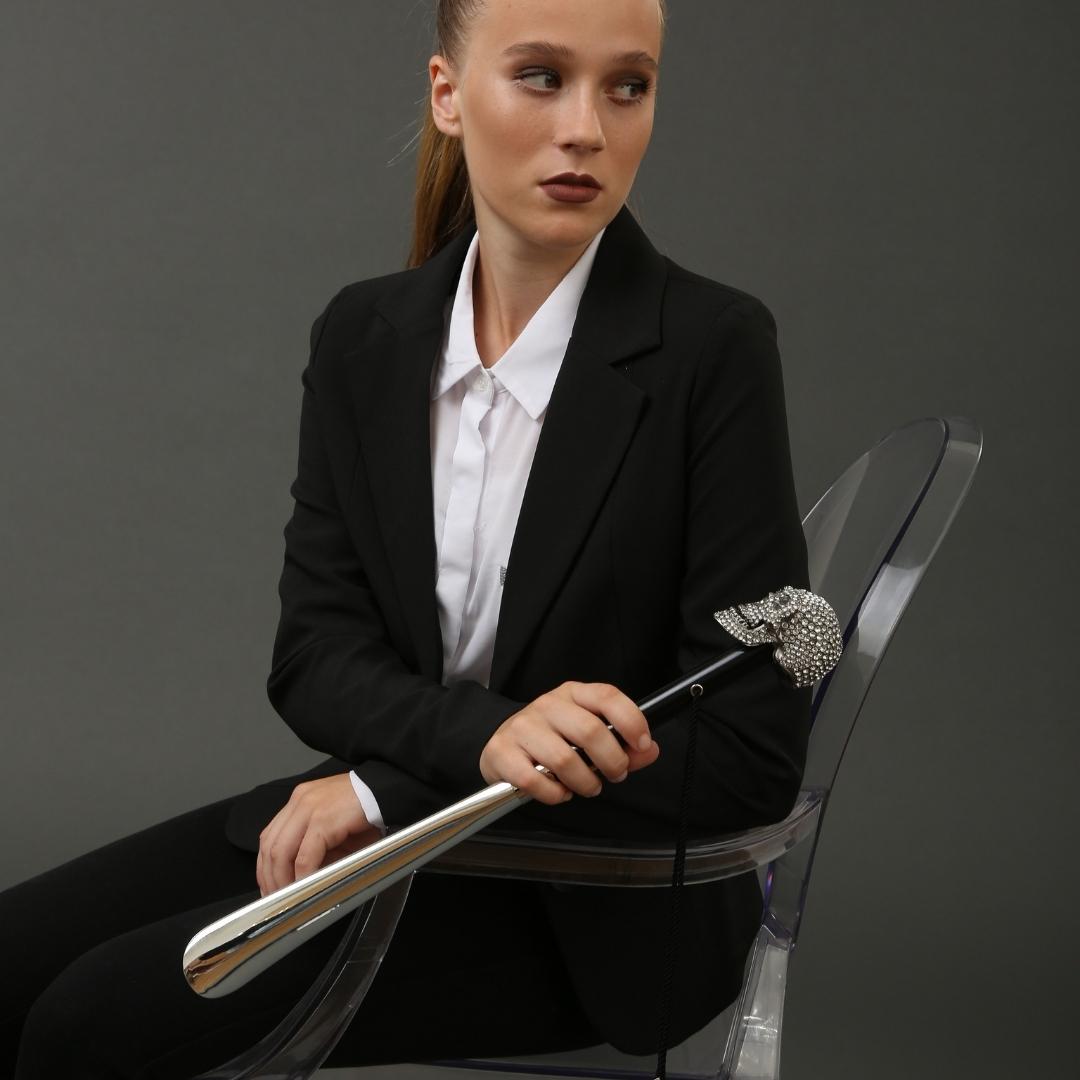 Woman in a black suit seated on a clear chair, holding the crystal skull shoehorn