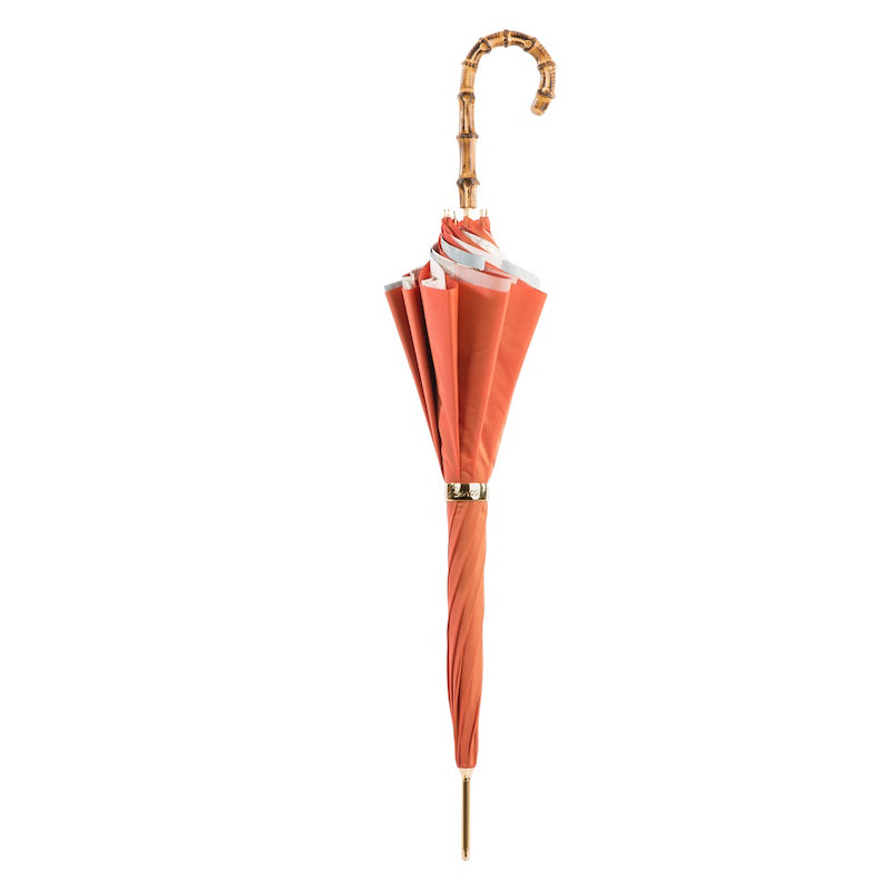 Closed coral umbrella standing upright with the bamboo crook handle and gold-tone ring