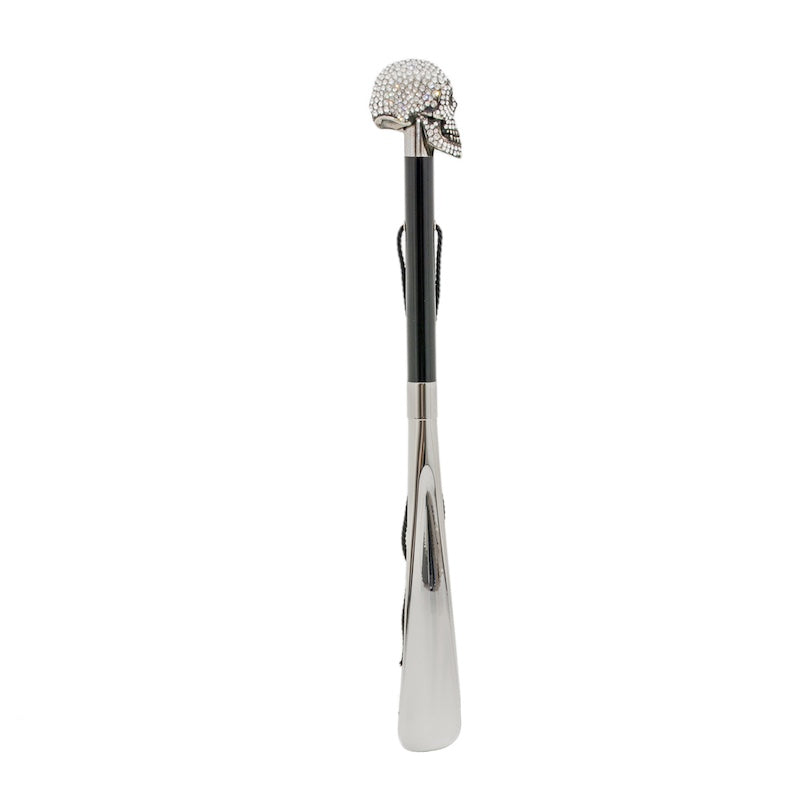 Skull shoehorn standing upright: glossy black shaft, hanging cord and silver-tone blade