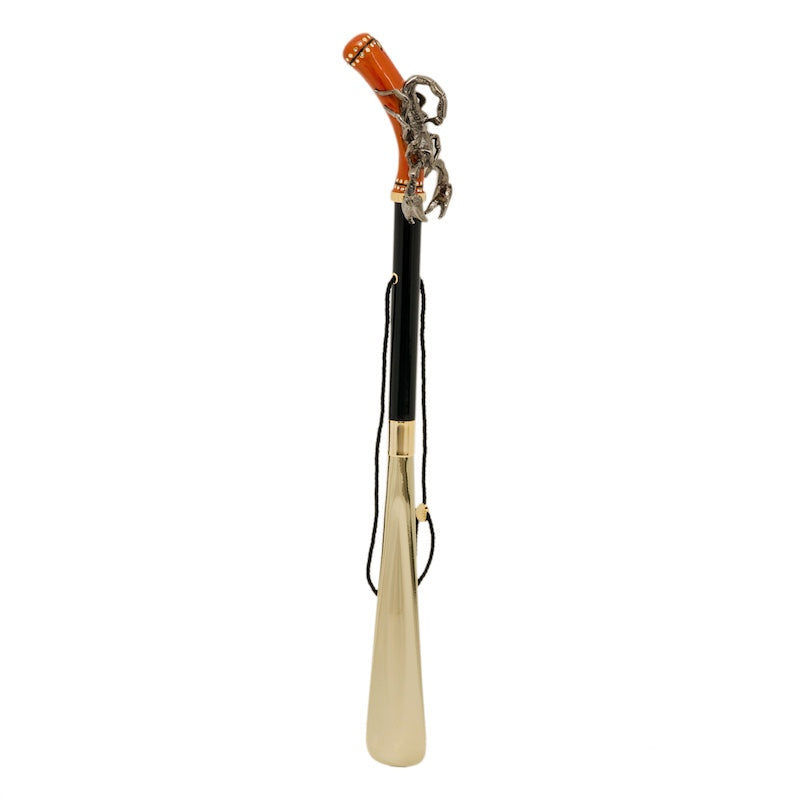 Scorpion shoehorn standing upright: ginger handle, glossy black shaft, cord and gold-tone blade
