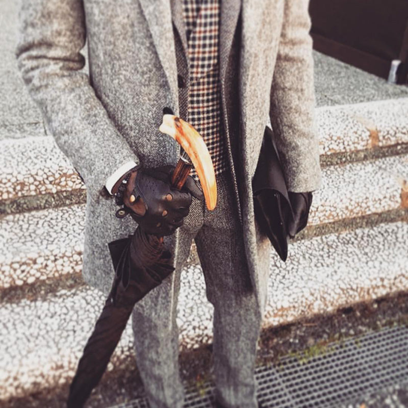 Man in a grey coat holding a furled umbrella by its warthog tusk handle