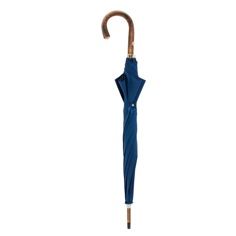 Closed blue umbrella standing upright with the chestnut crook handle