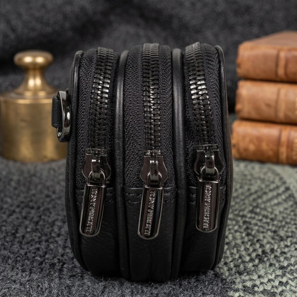 The three black-nickel zips of the black Tony Perotti clutch with branded Tony Perotti pullers