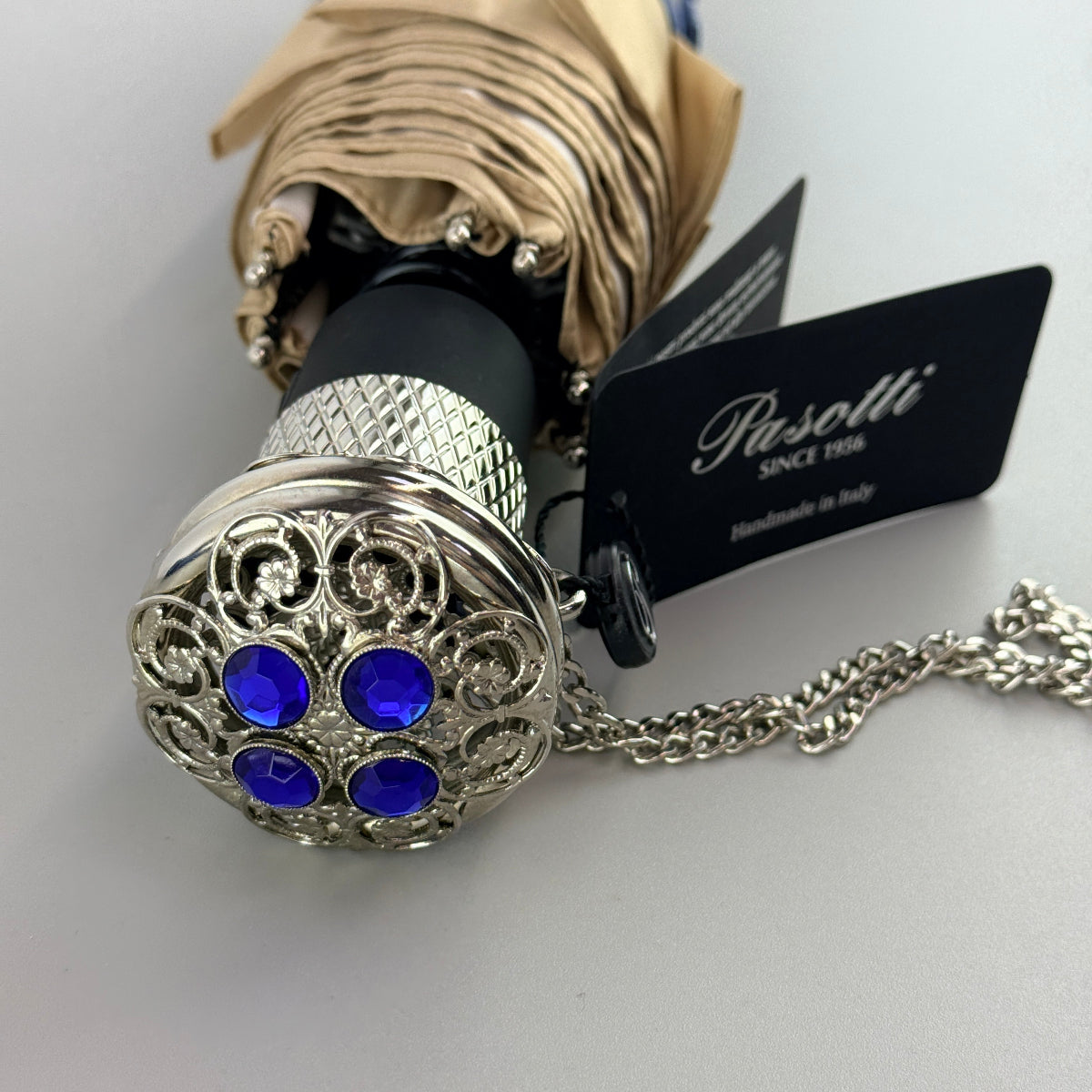 Decorative umbrella handle with blue gemstones and intricate design, featuring a Pasotti tag.