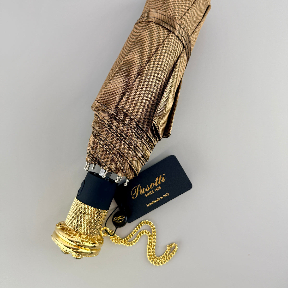 Foldable umbrella with gold handle and chain on a light gray background