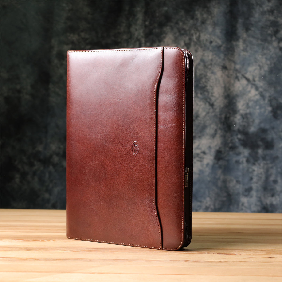 Dark brown Tony Perotti Italico 1278L padfolio handcrafted in Italy standing on a wooden desk — front with the embossed turtle emblem