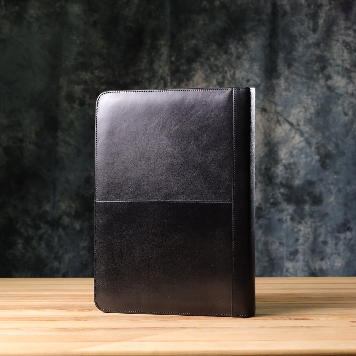 Back of the black Italico 1278L leather padfolio standing on a wooden desk — smooth glossy bull leather