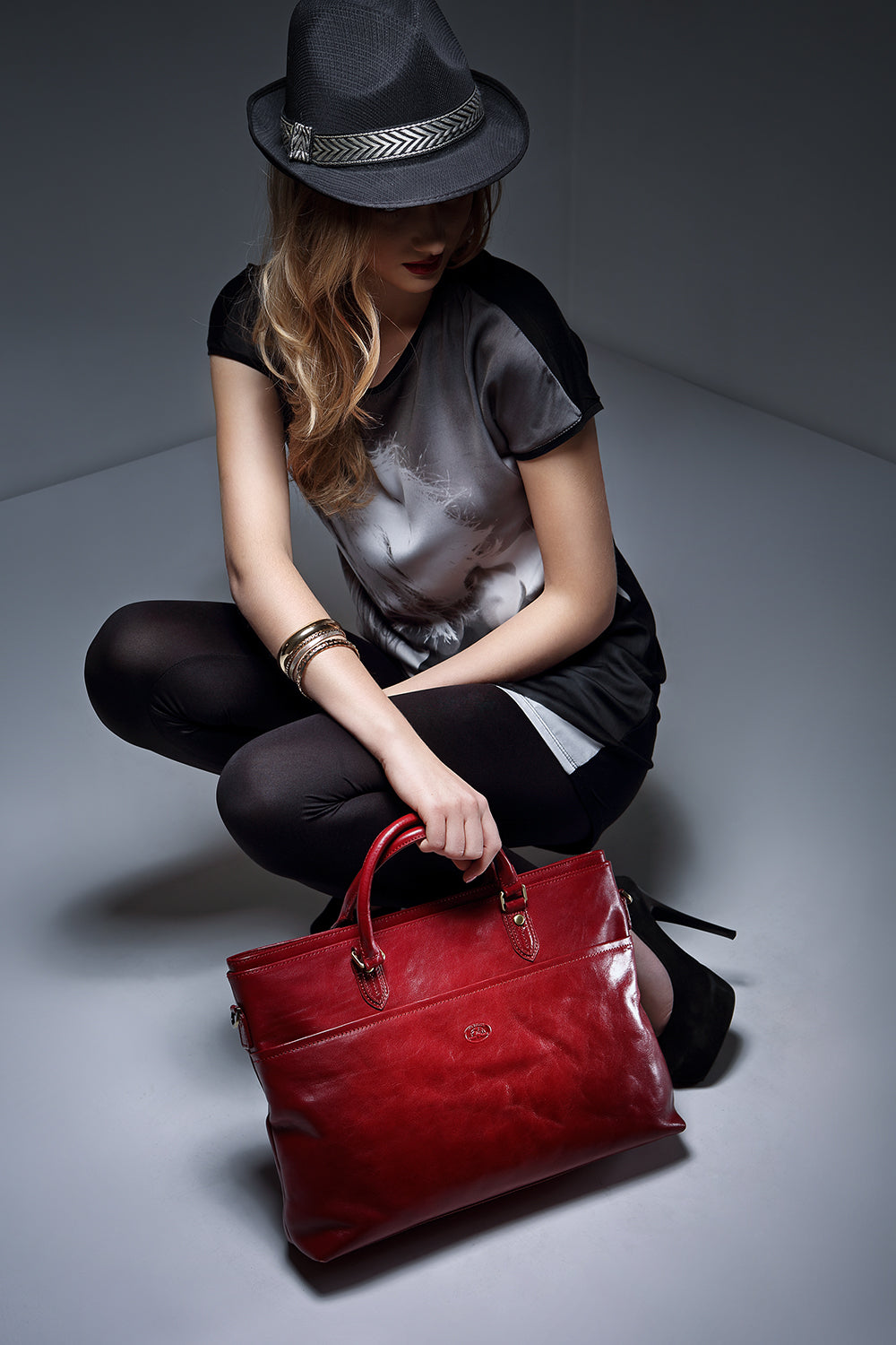 Woman seated on the floor holding the Tony Perotti Italico 7615 leather laptop bag by one handle (red colourway shown)