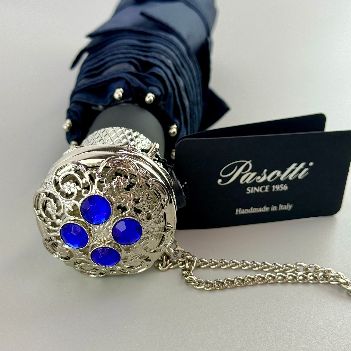 Decorative umbrella handle with blue stones and silver chain, featuring Pasotti brand on a white background.