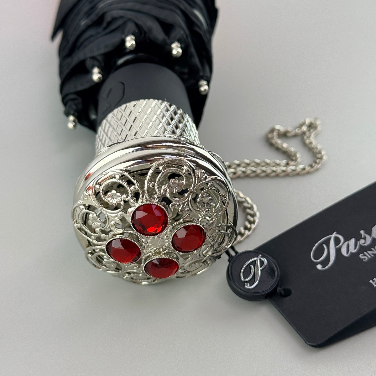 Pasotti decorative umbrella handle with red stones and silver filigree design on a white background