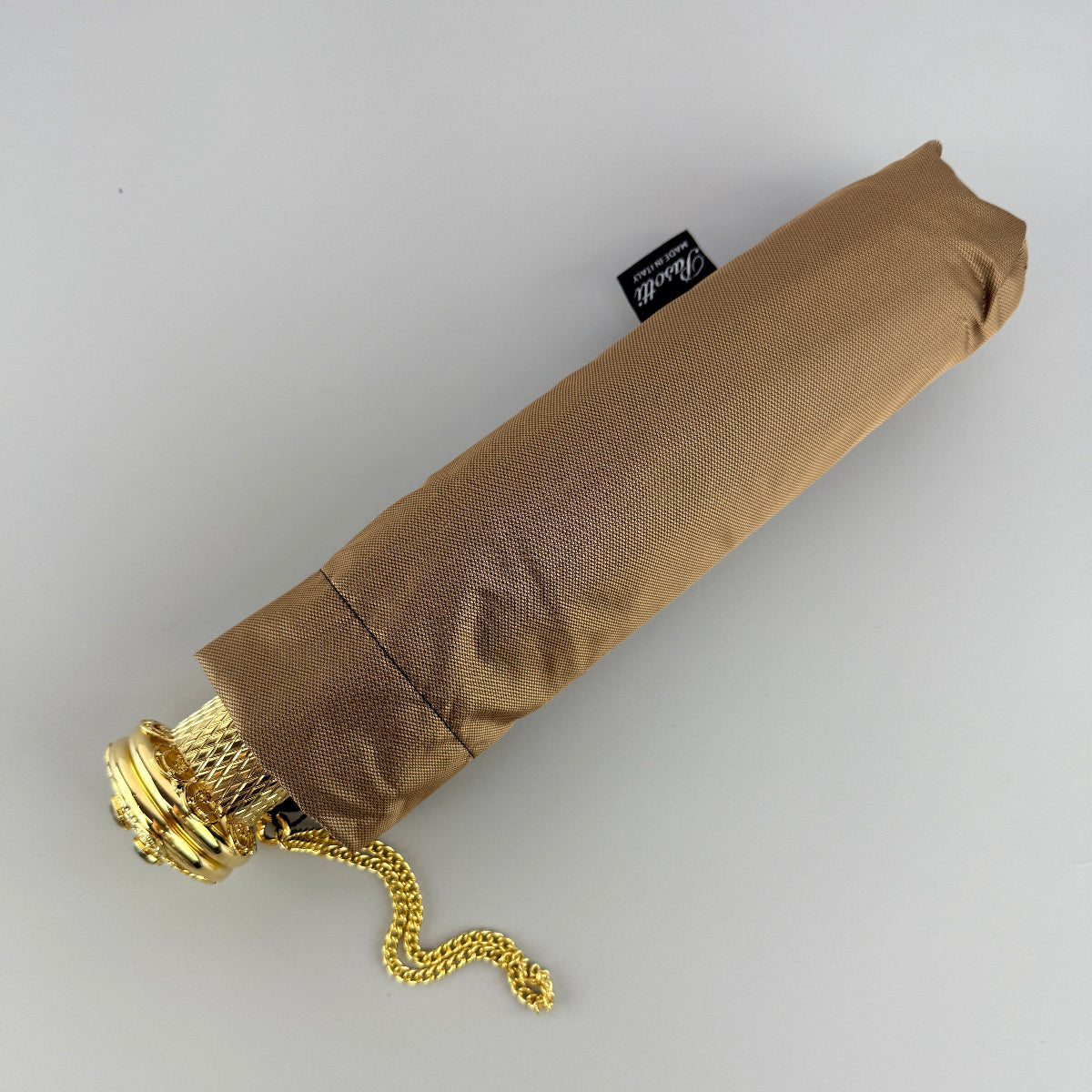 Pasotti folded beige umbrella with gold handle and shaft on a light gray background