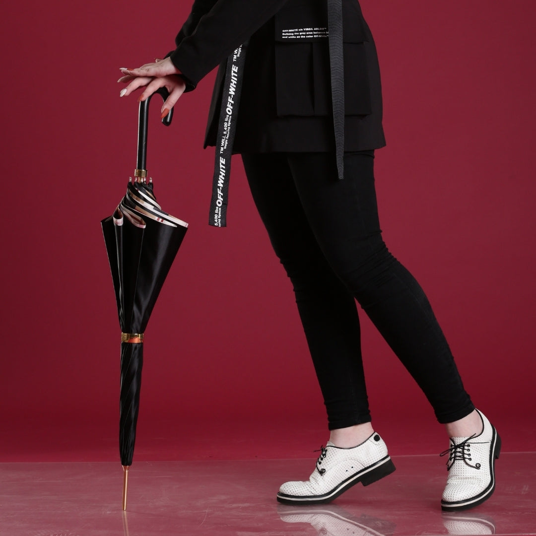 Person holding a black umbrella wearing a black outfit with white shoes on a red background