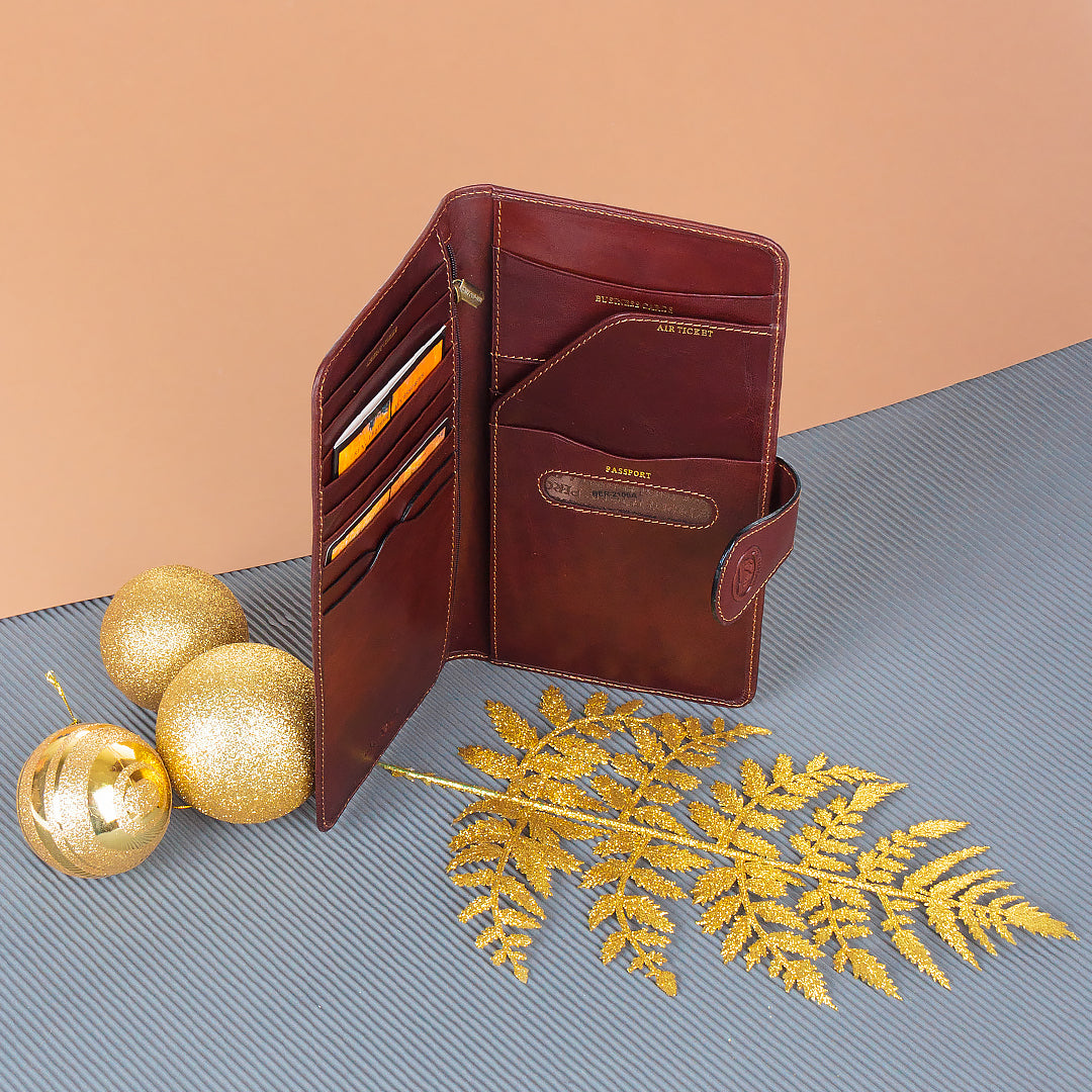 Brown leather travel wallet with gold accents on a textured surface with decorative elements.