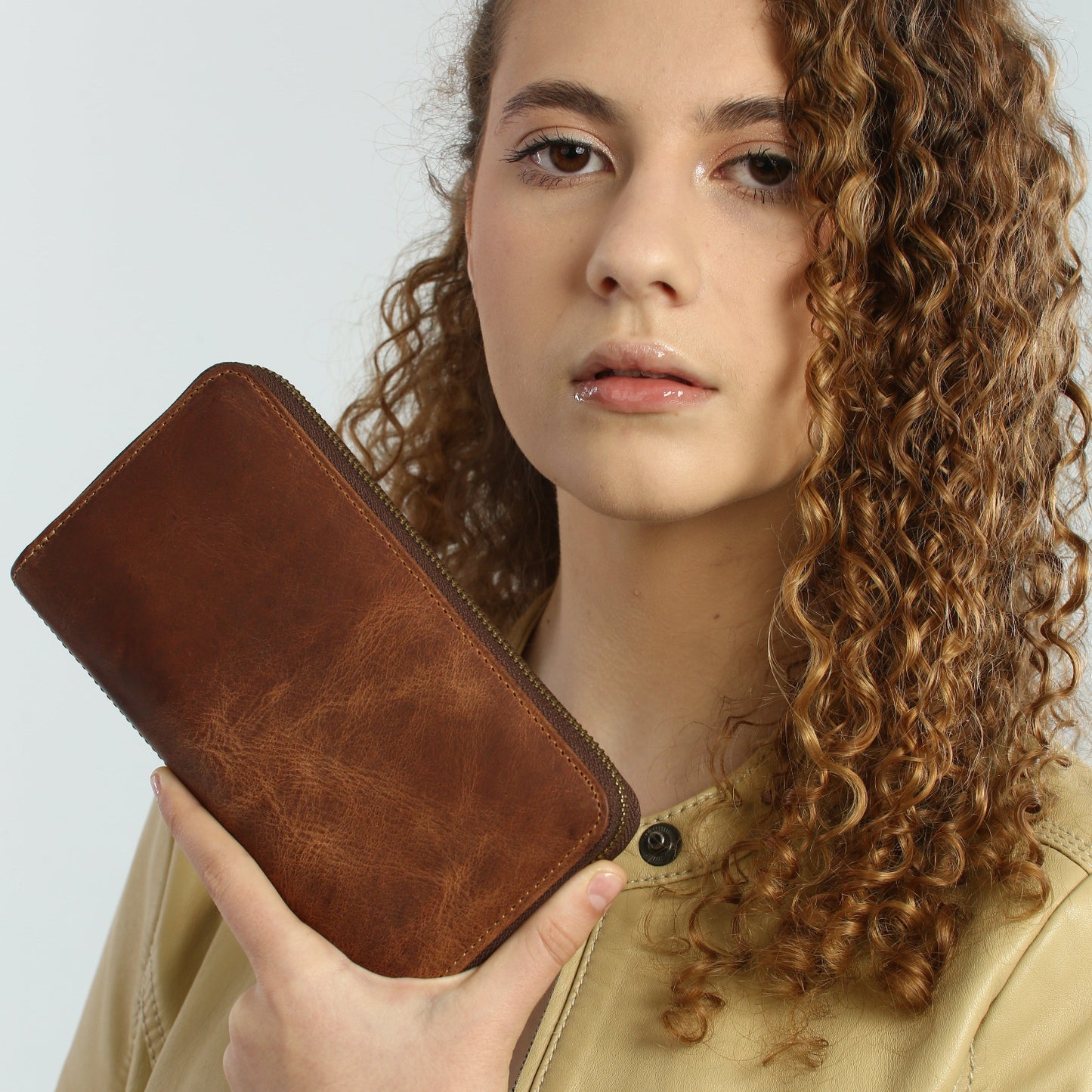 Woman holding a brown leather wallet against a plain background