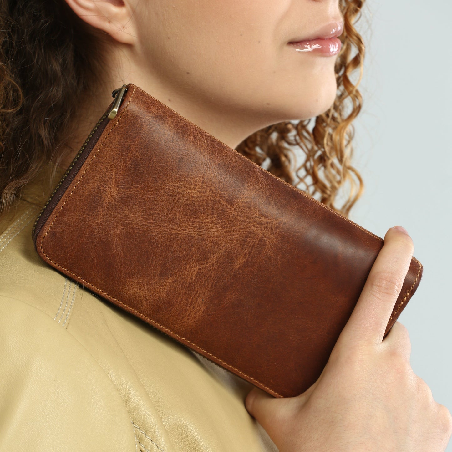 Brown leather wallet held by a person against a light blue background