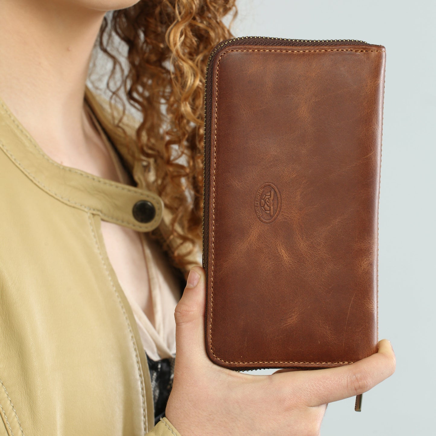 Person holding a brown leather wallet with a visible brand logo against a neutral background