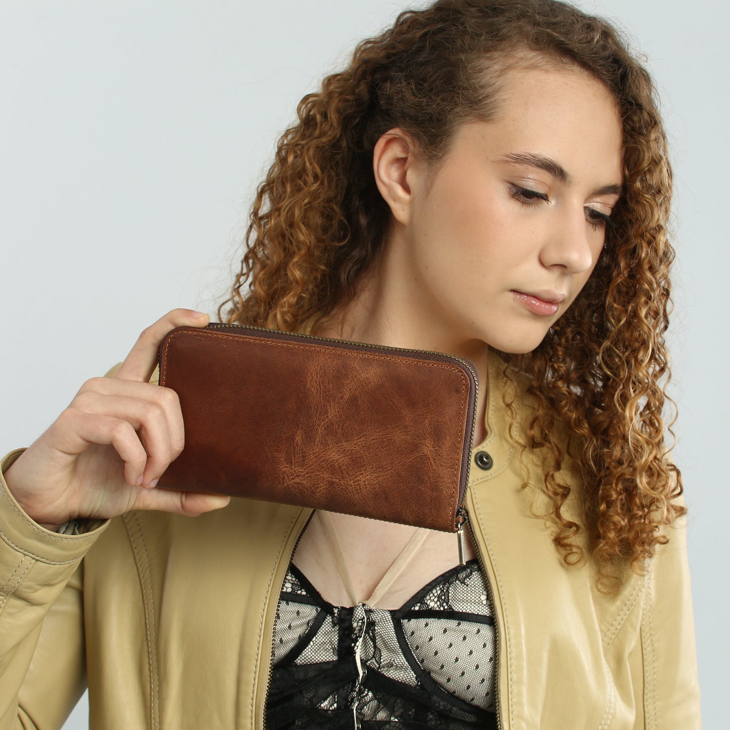 Woman holding a brown leather wallet against a plain background