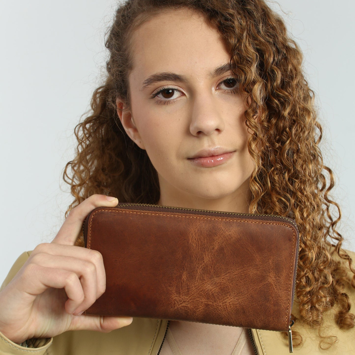 Woman holding a brown leather wallet against a plain background