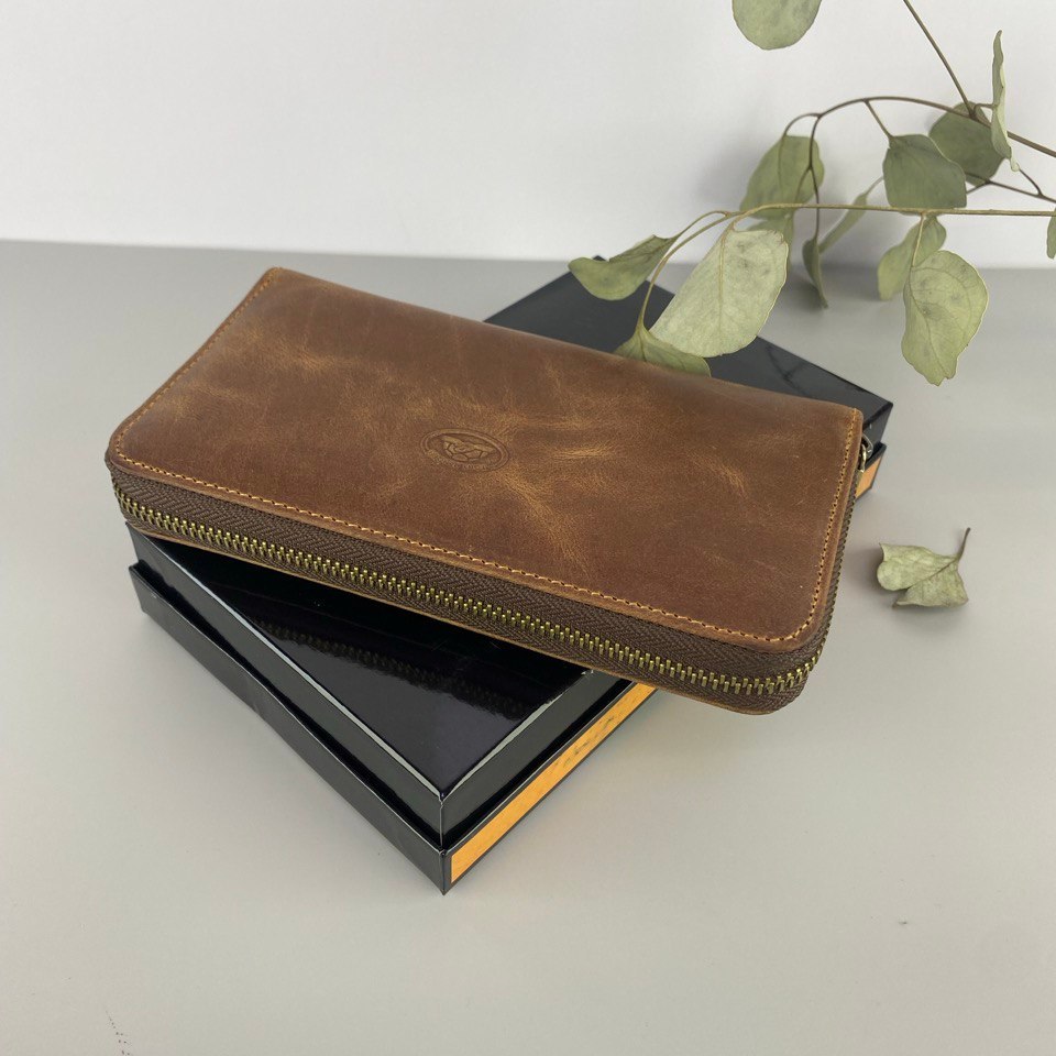 Brown leather wallet on a black box with green leaves in the background